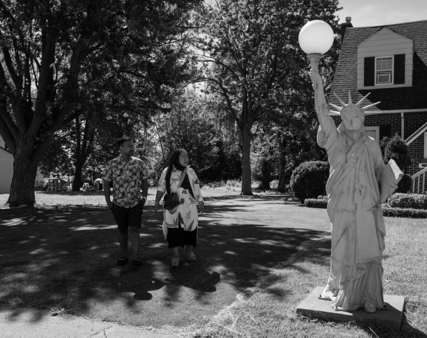 Black and white image of two people looking at statue of liberty replica on lawn